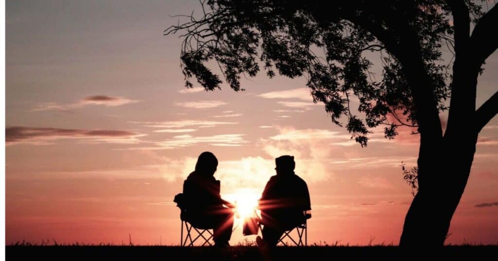 talking with loved one in camp chairs outdoors under tree at sunset