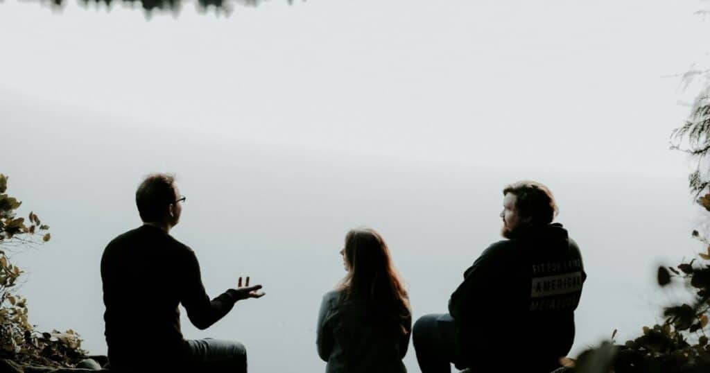 3 people having serious conversation by a lake